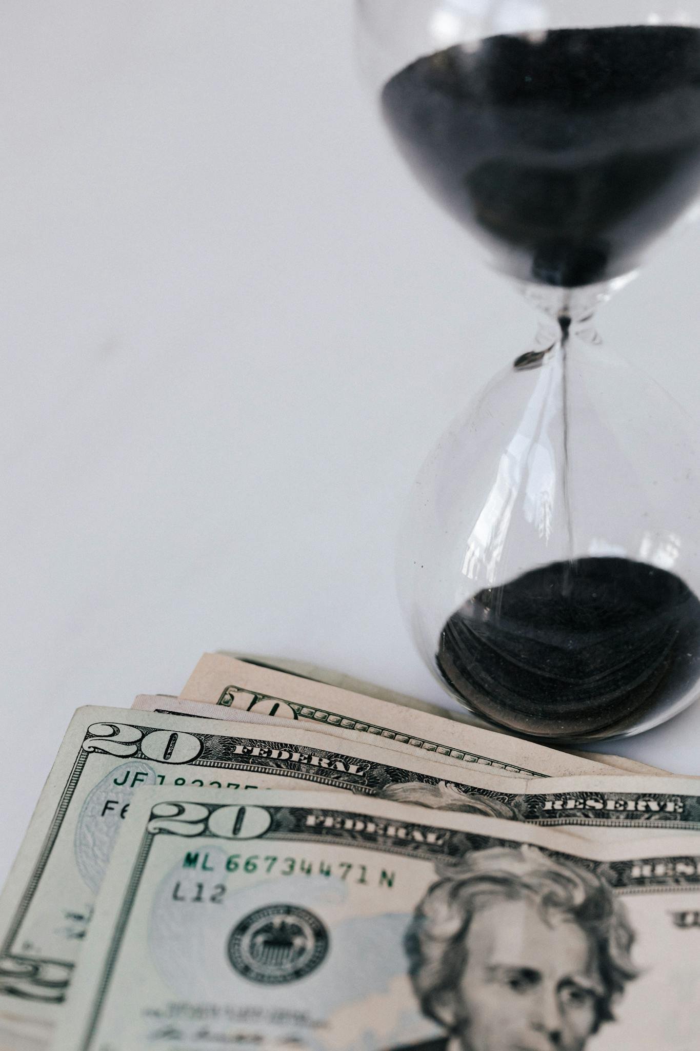 Close-up of an hourglass with dollar bills, symbolizing the connection between time and money.